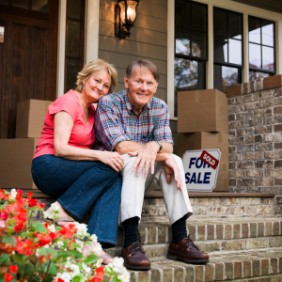 Senior Couple Sitting Outside House With For Sale Sign Senior couple preparing for move - moving help - potomac concierge