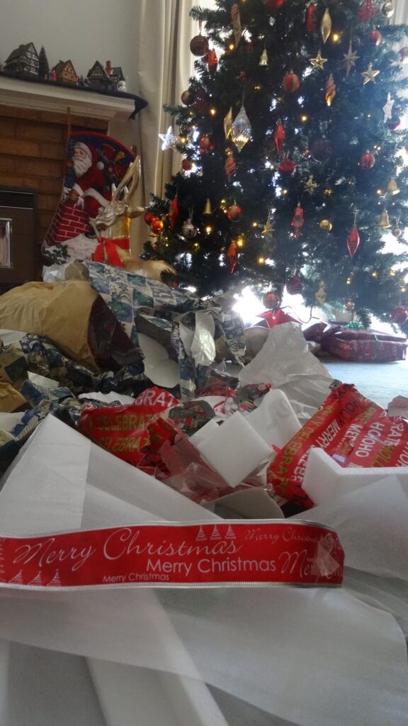 christmas tree with many open gifts and used wrapping paper and tissue papter around it