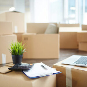 Accountant supplies Several unpacked carton boxes with office supplies, laptop, papers, calculator and green plant in flowerpot on top of packages