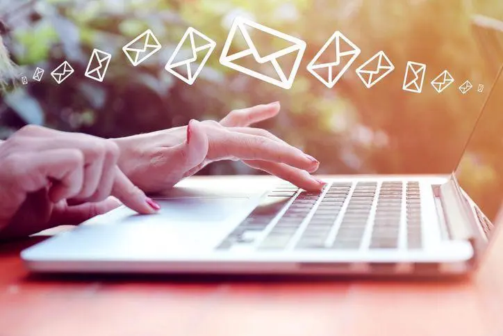 laptop open on table with womans hands typing and using the mouse with multiple mail icons floating