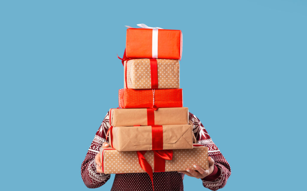 persons face is covered by stack of christmas presents they are holding with brown and red paper