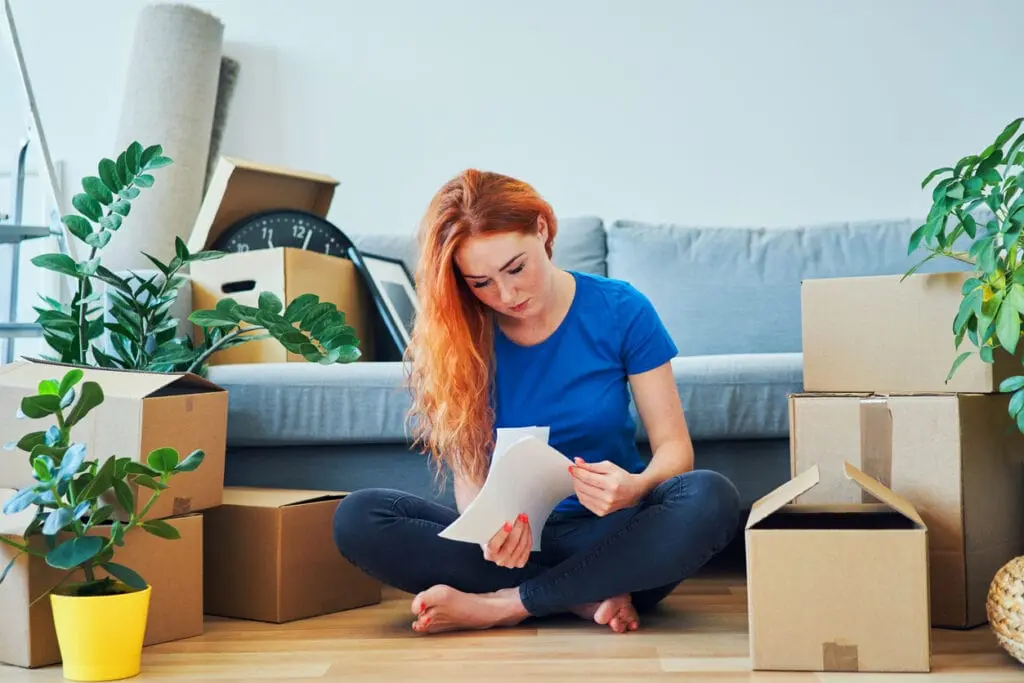 woman sitting on the floor looking at papers with moving boxes around her